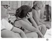 In der Hitze des Sommers sitzen drei Leute auf einen Häusersims, die in der Mitte Sitzende hält ihren Kopf gestützt.